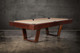 Doc & Holliday Zoey slate pool table, made in the USA, photographed at a three-quarter angle; tapered U-legs in warm maple, 1″ three-piece K-pattern slate, leather drop pockets, and mother-of-pearl sights styled as a modern lounge centerpiece. Doc & Holliday Zoey slate pool table, made in the USA, photographed at a three-quarter angle; tapered U-legs in warm maple, 1″ three-piece K-pattern slate, leather drop pockets, and mother-of-pearl sights styled as a modern lounge centerpiece.